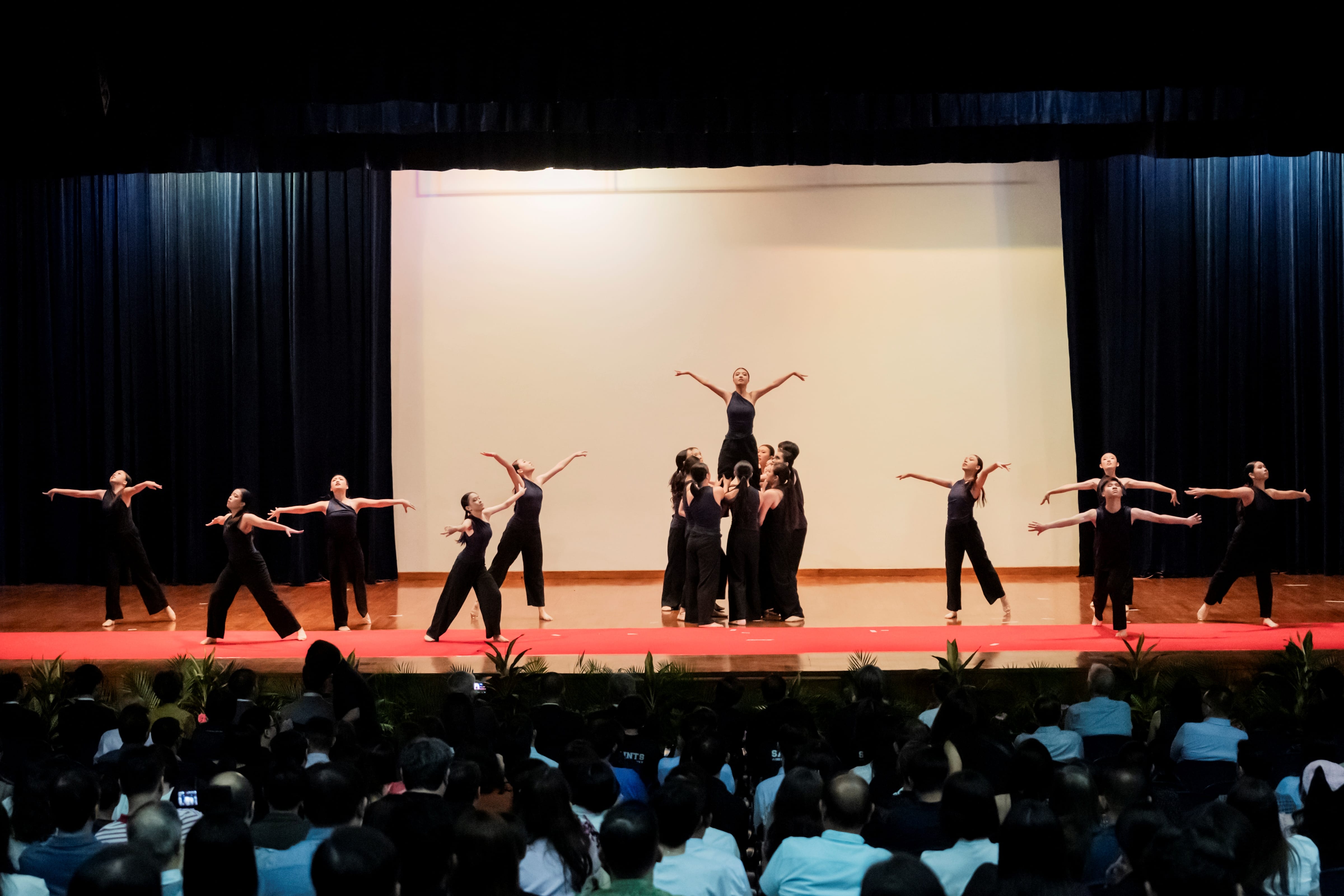 A group of dancing in different poses on stage, and one dancer who is lifted off the ground with her hands stretched out.